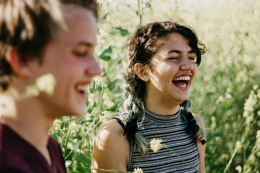 Two women laughing together in a sunlit meadow.